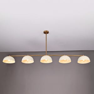 Op de afbeelding: Een moderne hanglamp met vijf lampen. Het heeft een messing afwerking en vijf crèmekleurige, koepelvormige kappen. De kappen zijn verdeeld over een horizontale balk. Een stijlvolle verlichtingsoplossing.
