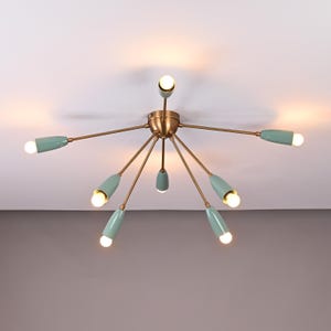 May include: A retro-style ceiling light fitting. The light has a brass-coloured central hub with multiple arms extending outwards. Each arm has a light blue, teardrop-shaped shade and a small, round light bulb. The fitting is mounted on a white ceiling.