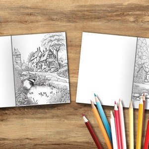 Puede incluir: Dos libros de colorear abiertos con ilustraciones en blanco y negro de un peque&ntilde;o pueblo con un puente y un estanque. Los libros est&aacute;n sobre una superficie de madera con l&aacute;pices de colores.