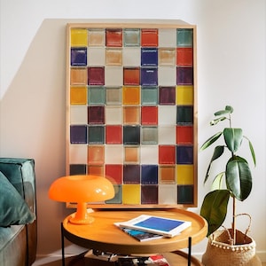 以下が含まれることがあります： 2段の木製コーヒーテーブル、本、オレンジ色のキノコ型ランプを備えたモダンなリビングルーム。カラフルなガラスブロックの額入りアートワークが壁に掛かっています。 植木鉢が隅にあります。