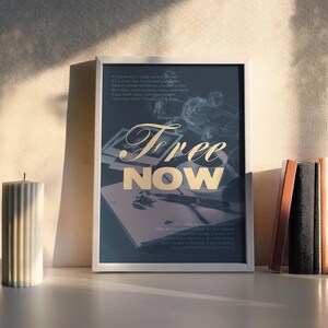 May include: A framed art print with the words "Free Now" in gold lettering. The print features a dark background with a notebook and pen, and a poem. A white candle and a stack of books are on the shelf.