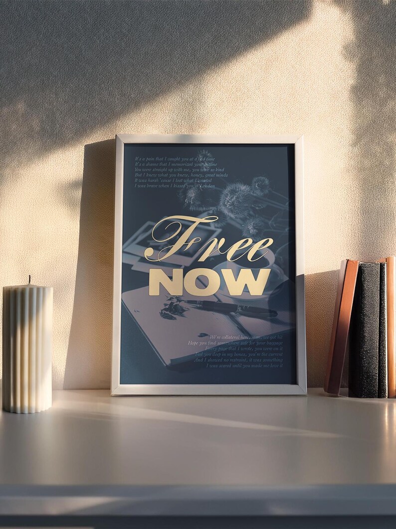 May include: A framed art print with the words "Free Now" in gold lettering. The print features a dark background with a notebook and pen, and a poem. A white candle and a stack of books are on the shelf.