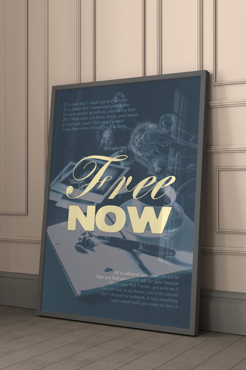 May include: Framed art print with the words "Free Now" in gold lettering. The print has a dark blue background with handwritten text and a pen and notebook visible. The frame is gray.