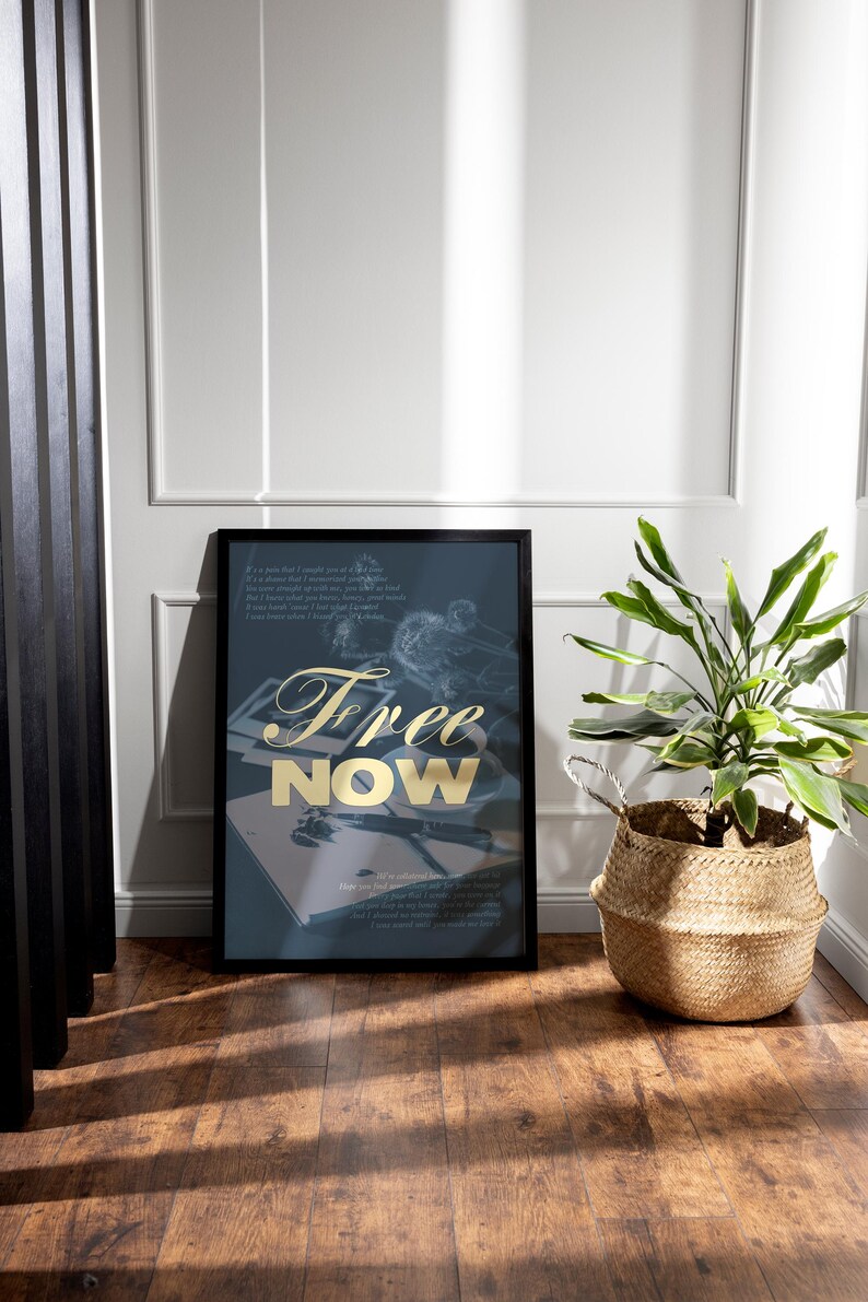 May include: A framed art print with the words "Free Now" in gold lettering. The print is on a dark blue background with a faded illustration. A potted plant in a woven basket sits nearby.