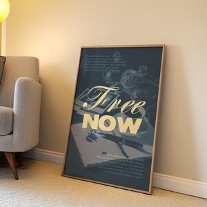 May include: A framed art print with the words "Free Now" in gold script. The artwork features a dark blue background with a still life of a pen, notebook, and flowers. The print is leaning against a wall.