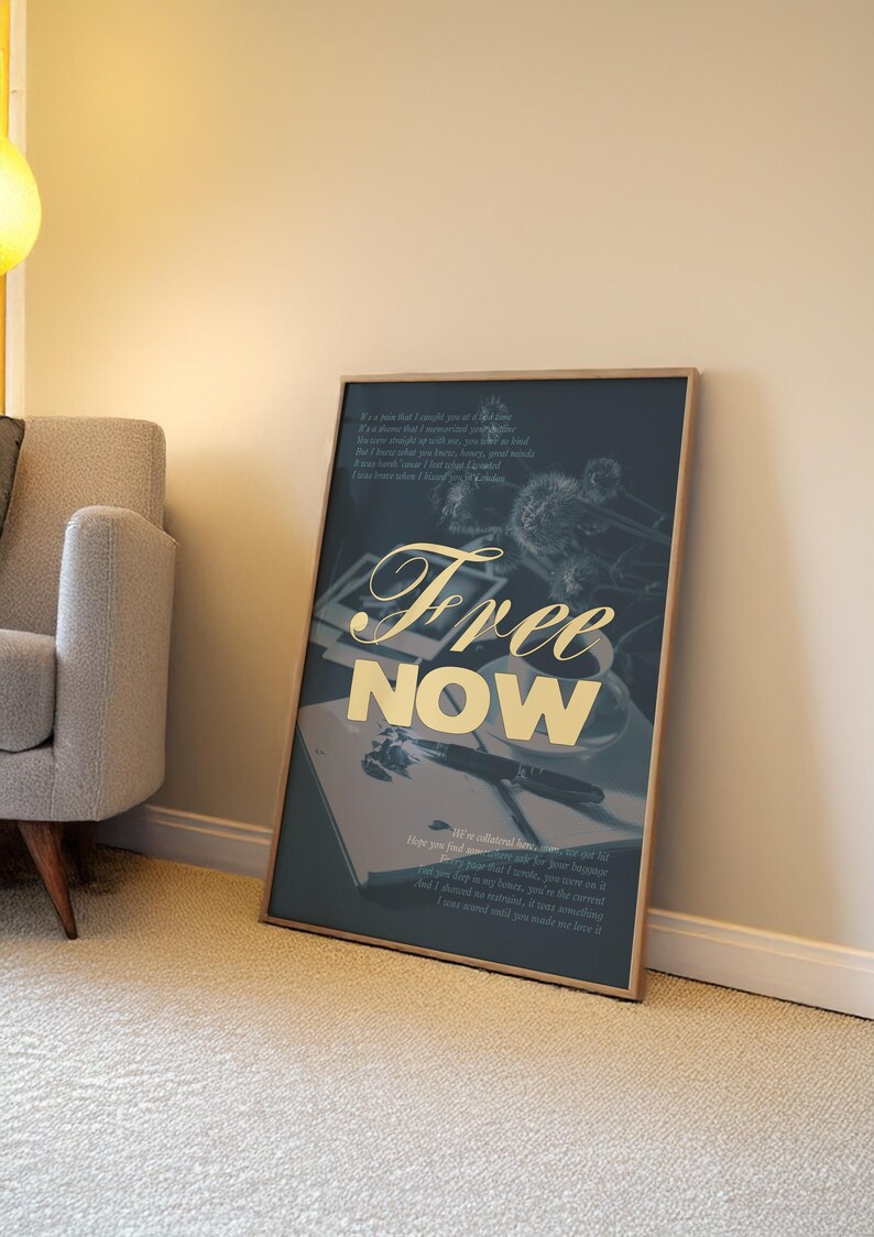 May include: A framed art print with the words "Free Now" in gold script. The artwork features a dark blue background with a still life of a pen, notebook, and flowers. The print is leaning against a wall.