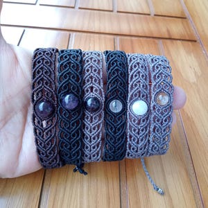 Könnte beinhalten: Sechs geflochtene Armbänder mit verschiedenen Schnüren und Edelsteinperlen. Die Armbänder sind braun, schwarz und grau. Die Perlen sind Amethyst, klar und weiß.