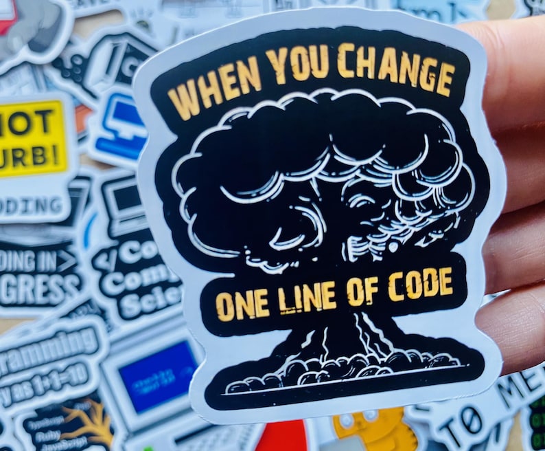 Może przedstawiać: Biała naklejka z czarno-białym rysunkiem eksplodującego grzyba atomowego. Naklejka zawiera napis "WHEN YOU CHANGE ONE LINE OF CODE" w kolorze ż&oacute;łtym.
