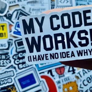 Może przedstawiać: Biała naklejka z czarnym tekstem, kt&oacute;ry brzmi "My Code Works! (I Have No Idea Why)". Naklejkę trzyma ręka.