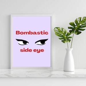 Peut inclure: Une impression encadrée blanche avec un fond violet clair. L'impression présente le texte "Bombastic side eye" en lettres rouges et une paire d'yeux noirs avec un eye-liner regardant sur le côté.