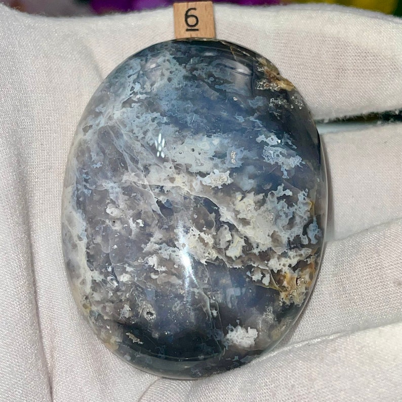 May include: A smooth, oval-shaped, polished stone with a swirling pattern of gray, white, and black. The stone has a glossy finish.