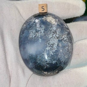 May include: A smooth, round, gray and white agate stone with a swirling pattern. The stone is labeled with the number "5".