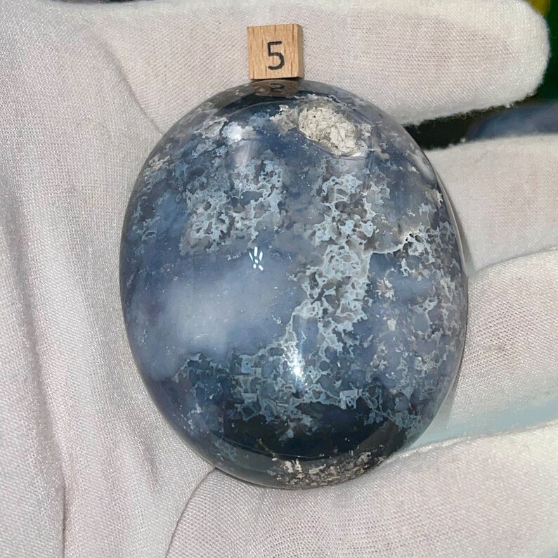 May include: A smooth, round, gray and white agate stone with a swirling pattern. The stone is labeled with the number "5".