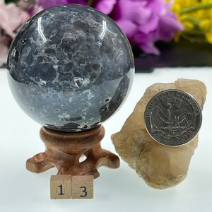 May include: A black and white agate sphere on a wooden stand. The sphere is approximately 1.5 inches in diameter. The sphere is next to a small piece of clear quartz. The numbers 1 and 3 are visible on the bottom of the image.