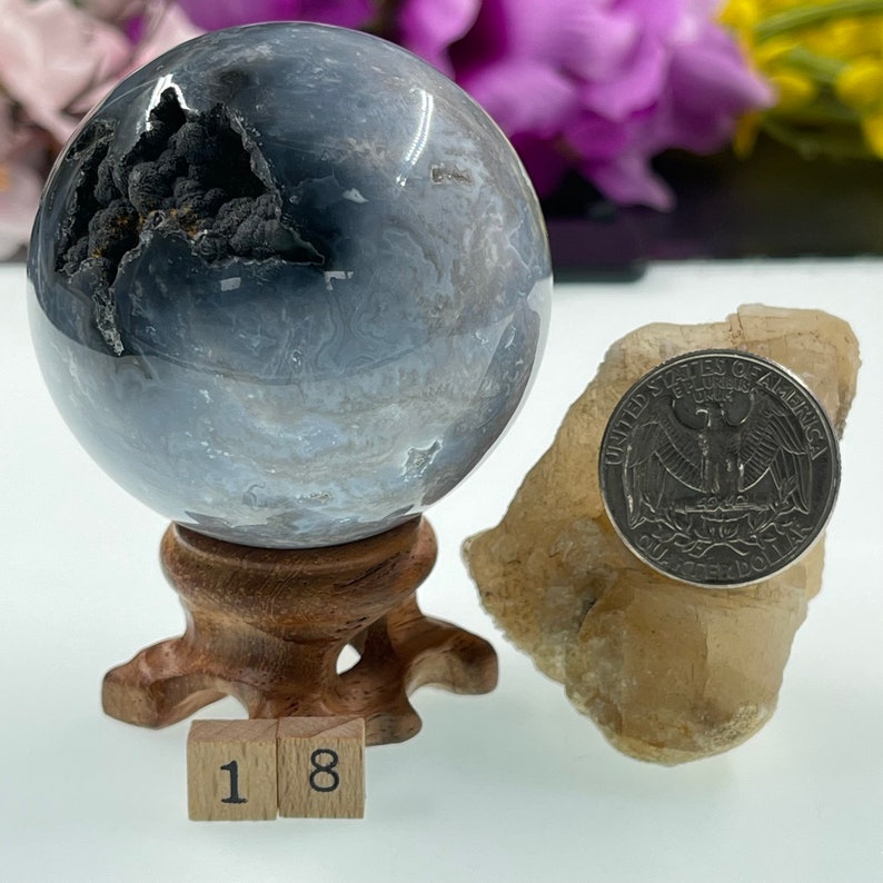 May include: A grey and white agate sphere with black inclusions, displayed on a wooden stand. The sphere is approximately 5 cm in diameter. A US quarter is included for scale.