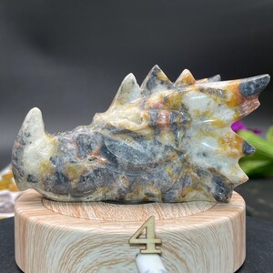 May include: A carved dragon sculpture made of white, gray, and orange marble. The dragon is lying on its side with its head raised and its wings spread out. The sculpture is sitting on a wooden base with the number "4" written on it.