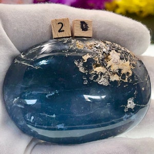 May include: A smooth, dark blue and white agate stone with a polished finish. The stone is oval shaped and has a natural, organic pattern. The stone is labeled with the number "2D".