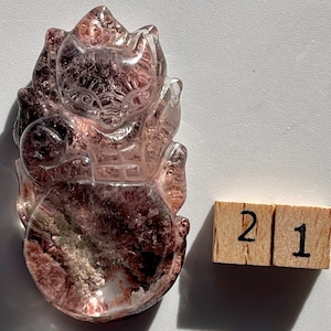 Può includere: Una scultura in quarzo trasparente di una creatura mitologica con inclusioni rosa e marroni. La scultura è alta circa 5 cm.