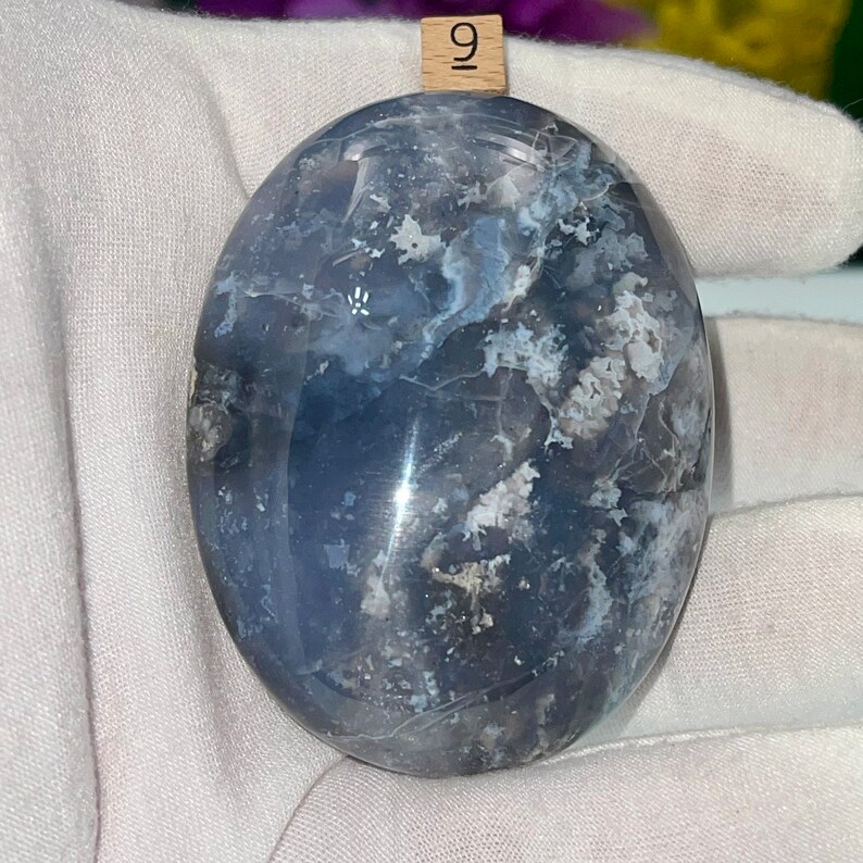 May include: A smooth, polished blue agate stone with white and gray markings. The stone is oval shaped and has a glossy finish.