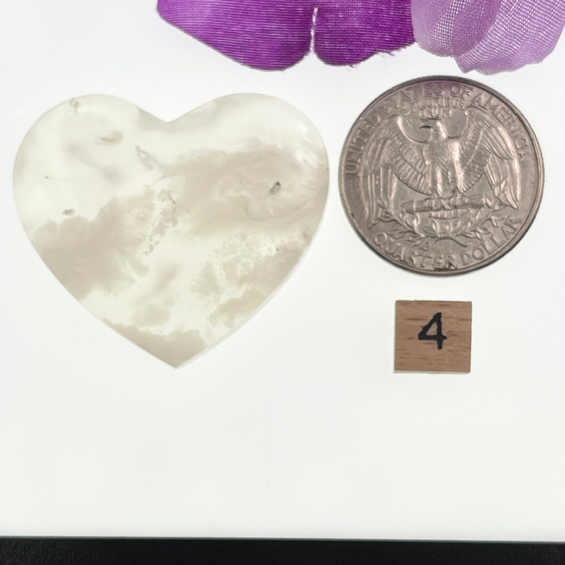 May include: White heart-shaped agate with a cloudy pattern, next to a US quarter and a wooden block with the number 4 printed on it.