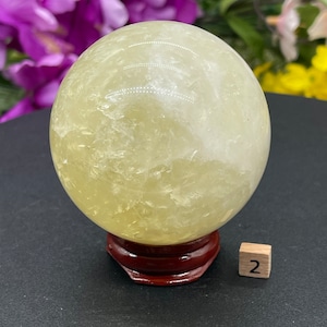 May include: A large, yellow citrine crystal sphere on a wooden stand. The sphere is approximately 2 inches in diameter.