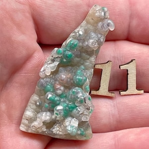 May include: A close-up of a green and white agate with a unique, bubbly texture. The agate is approximately 5 cm tall and is resting on a hand.