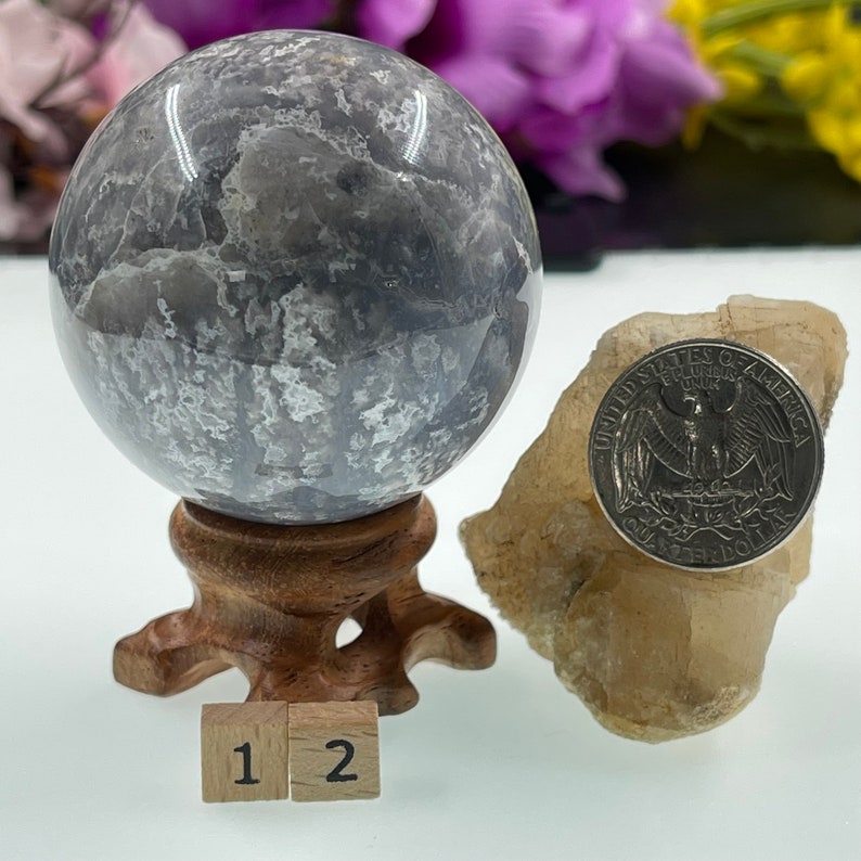 May include: A grey and white agate sphere on a wooden stand with a US quarter for scale. The sphere is approximately 5 cm in diameter.