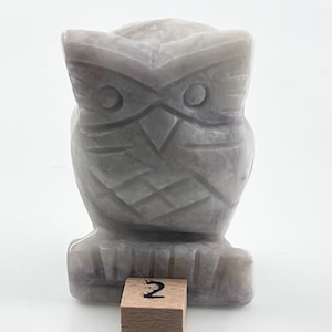 Op de afbeelding: Een grijs, gegraveerd uilenbeeldje van steen. De uil zit op een houten blok met het nummer "2" erop.