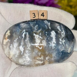 May include: A smooth, oval-shaped agate stone with a swirling pattern of white, gray, and blue. The stone is labeled with the numbers "3" and "4".