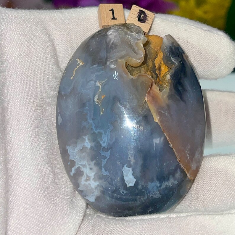 May include: A smooth, gray and white agate stone with a natural, irregular shape. The stone has a light brown, almost translucent section on one side.
