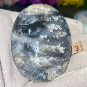 May include: A smooth, polished, gray and white agate stone with a swirling pattern. The stone is about 2 inches in diameter.