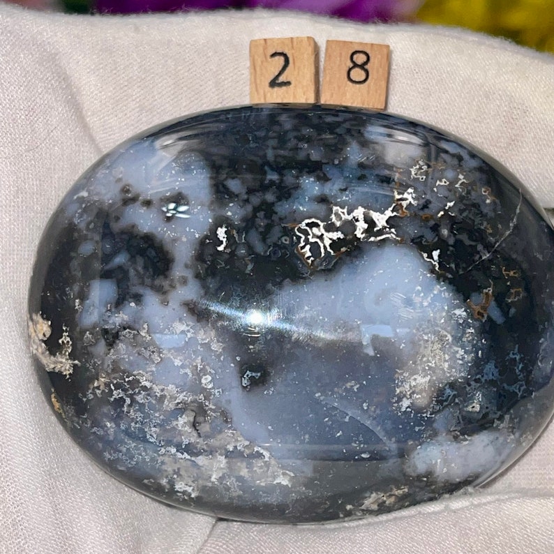 K&ouml;nnte beinhalten: Ein polierter, ovaler, schwarz-wei&szlig;er Achat-Stein mit einem wirbelnden Muster. Der Stein hat einen Durchmesser von etwa 7,1 cm.