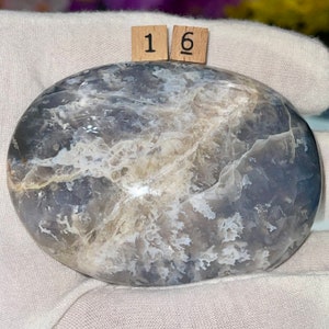 May include: A smooth, oval-shaped, polished stone with a swirling pattern of gray, white, and light blue. The stone is labeled with the number "16".