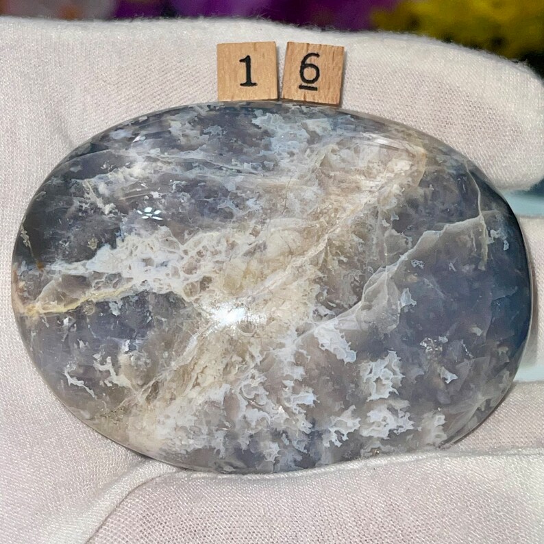May include: A smooth, oval-shaped, polished stone with a swirling pattern of gray, white, and light blue. The stone is labeled with the number "16".