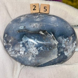 K&ouml;nnte beinhalten: Ein glatter, ovaler blauer Achat-Stein mit wei&szlig;en und grauen Markierungen. Der Stein ist poliert und hat eine gl&auml;nzende Oberfl&auml;che. Die Zahlen "25" sind auf zwei kleinen Holzbl&ouml;cken geschrieben.