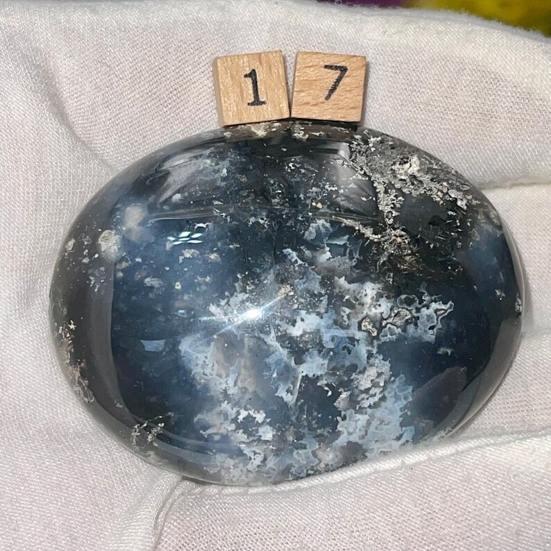 May include: A smooth, gray and white agate stone with a swirling pattern. The stone is polished and has a glossy finish. The stone is labeled with the number "17".