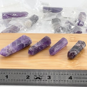 May include: Four amethyst crystal points, each with a different shade of purple, are arranged on a wooden surface. A ruler is visible in the bottom of the image, with markings in inches.