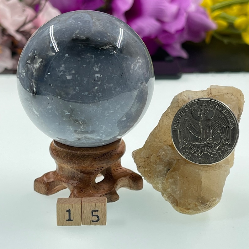 May include: A grey and white agate sphere on a wooden stand with a 25 cent coin for scale. The sphere is approximately 3.8 cm in diameter. The sphere is a natural stone and has a unique pattern.