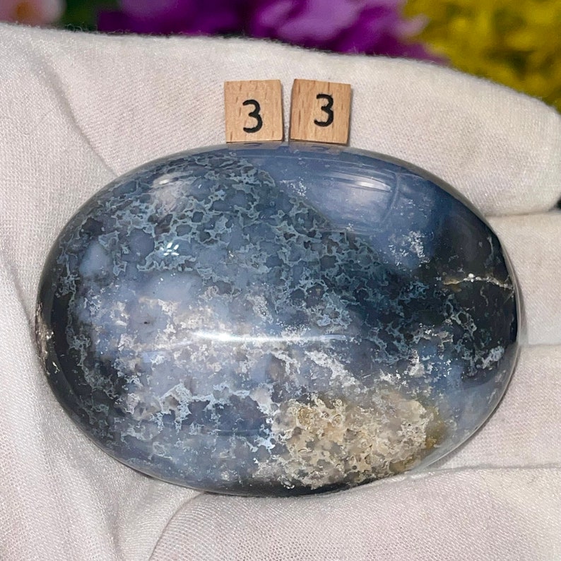 May include: A smooth, gray and white agate stone with a mottled pattern. The stone is oval shaped and has a polished finish. The stone is labeled with the number "33".