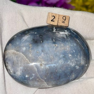 K&ouml;nnte beinhalten: Ein glatter, ovaler blauer Achat-Stein mit wei&szlig;en und grauen Wirbeln und Markierungen. Der Stein hat einen Durchmesser von etwa 7,4 cm.