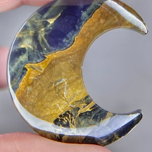 May include: A crescent moon shaped piece of polished agate with a blue, gold, and black pattern.