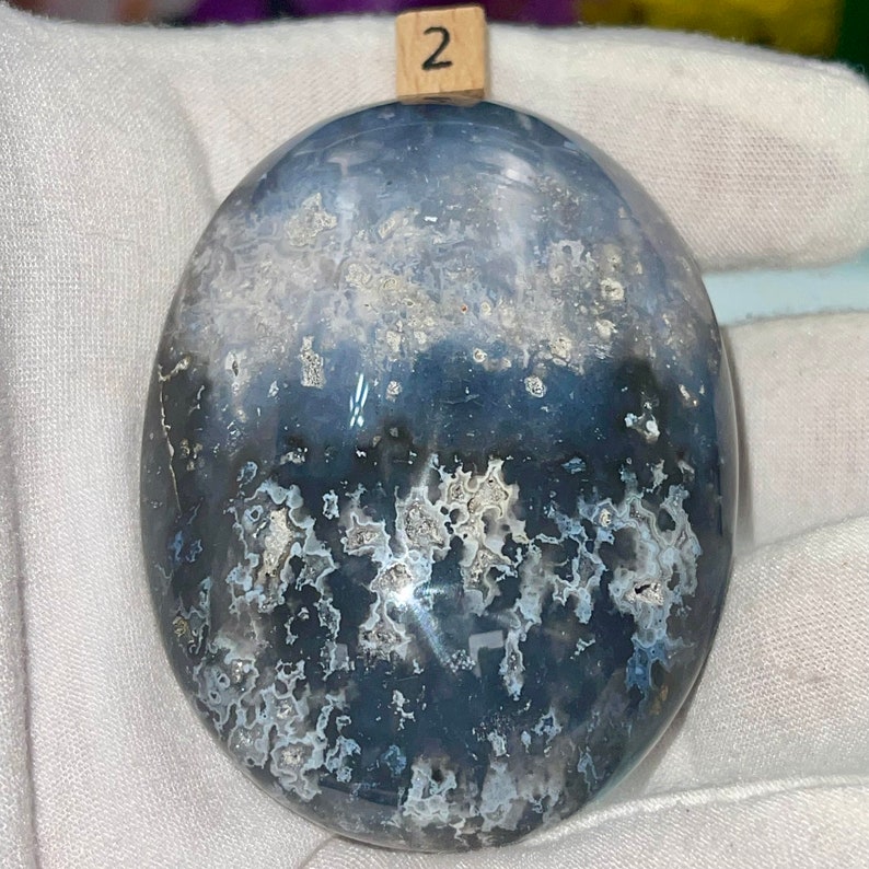 May include: A smooth, polished, gray and white agate stone with a swirling pattern. The stone is shaped like an oval and has a glossy finish.