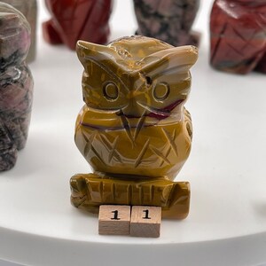 Op de afbeelding: Een gesneden uilbeeldje van gele en rode jaspis. De uil zit op een houten voet met het nummer "11" erop.