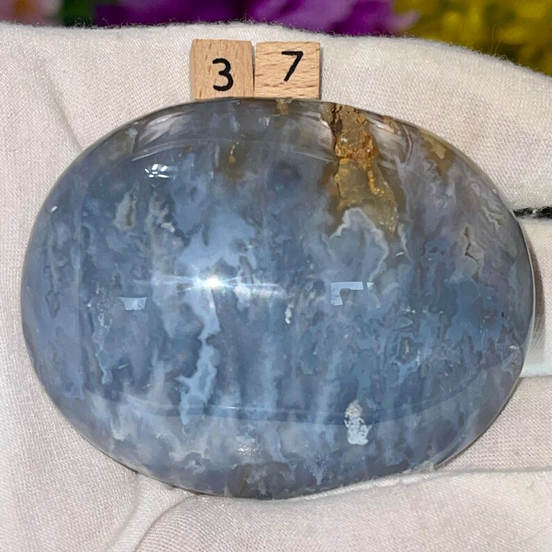 May include: A smooth, polished blue agate stone with white and brown markings. The stone is oval shaped and has a glossy finish.