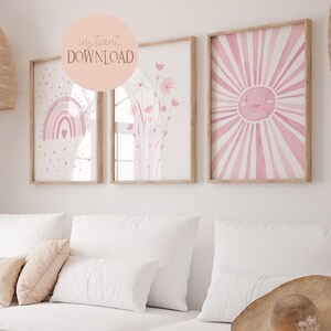 Könnte beinhalten: Drei rosa und weiße Aquarelldrucke in Holzrahmen. Die Drucke zeigen einen Regenbogen mit Herzen, einen Blumenstrauß und eine lächelnde Sonne mit rosa Strahlen.