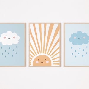 May include: Three framed prints with a blue sky background. The left and right prints feature a white and blue cloud with a smiling face and raindrops falling from it. The centre print features a yellow sun with a smiling face and orange and yellow rays.