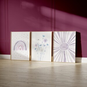 Könnte beinhalten: Drei gerahmte Aquarelldrucke in einem lila und weißen Farbschema. Die Drucke zeigen einen Regenbogen mit einem Herzen, einen Blumenstrauß und eine Sonne mit einem lächelnden Gesicht.
