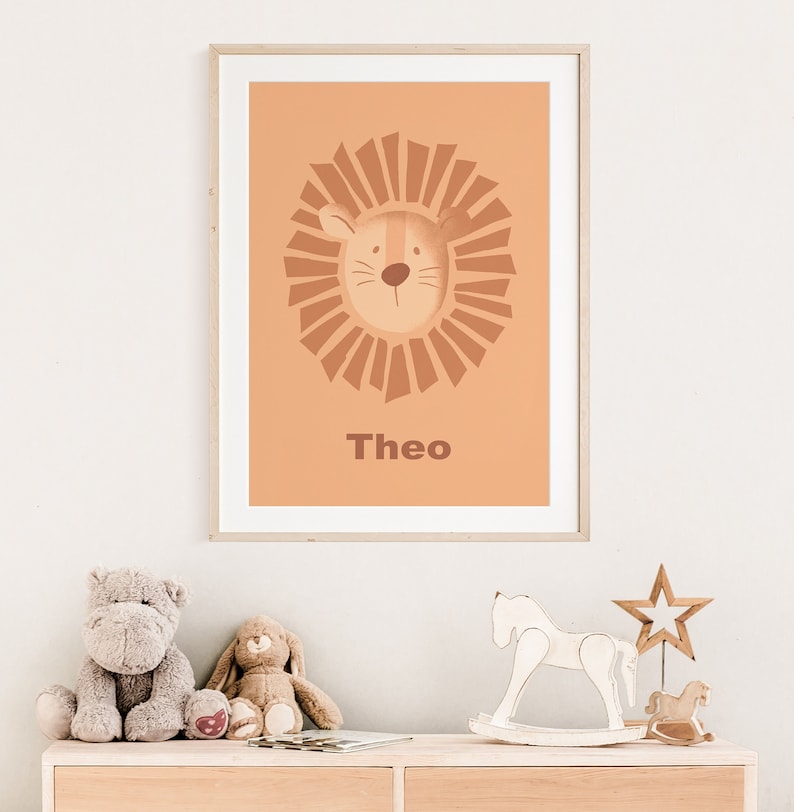 K&ouml;nnte beinhalten: Ein gerahmter Druck mit einem Cartoon-L&ouml;wenkopf in einer braunen M&auml;hne auf einem pfirsichfarbenen Hintergrund. Der Name "Theo" ist unter dem L&ouml;wen gedruckt.