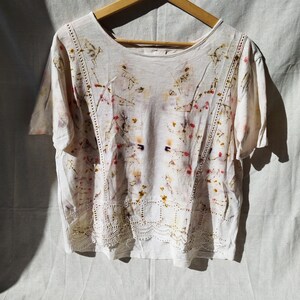 Puede incluir: Una camiseta de algodón blanca con estampado floral y ribete de encaje. La camiseta tiene un corte holgado y mangas cortas.