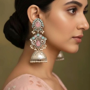 May include: Silver-toned earrings with pink and turquoise gemstones and small white pearls. The earrings have a tiered design, with a bell-shaped bottom and intricate detailing. The gemstones are teardrop and oval shaped.